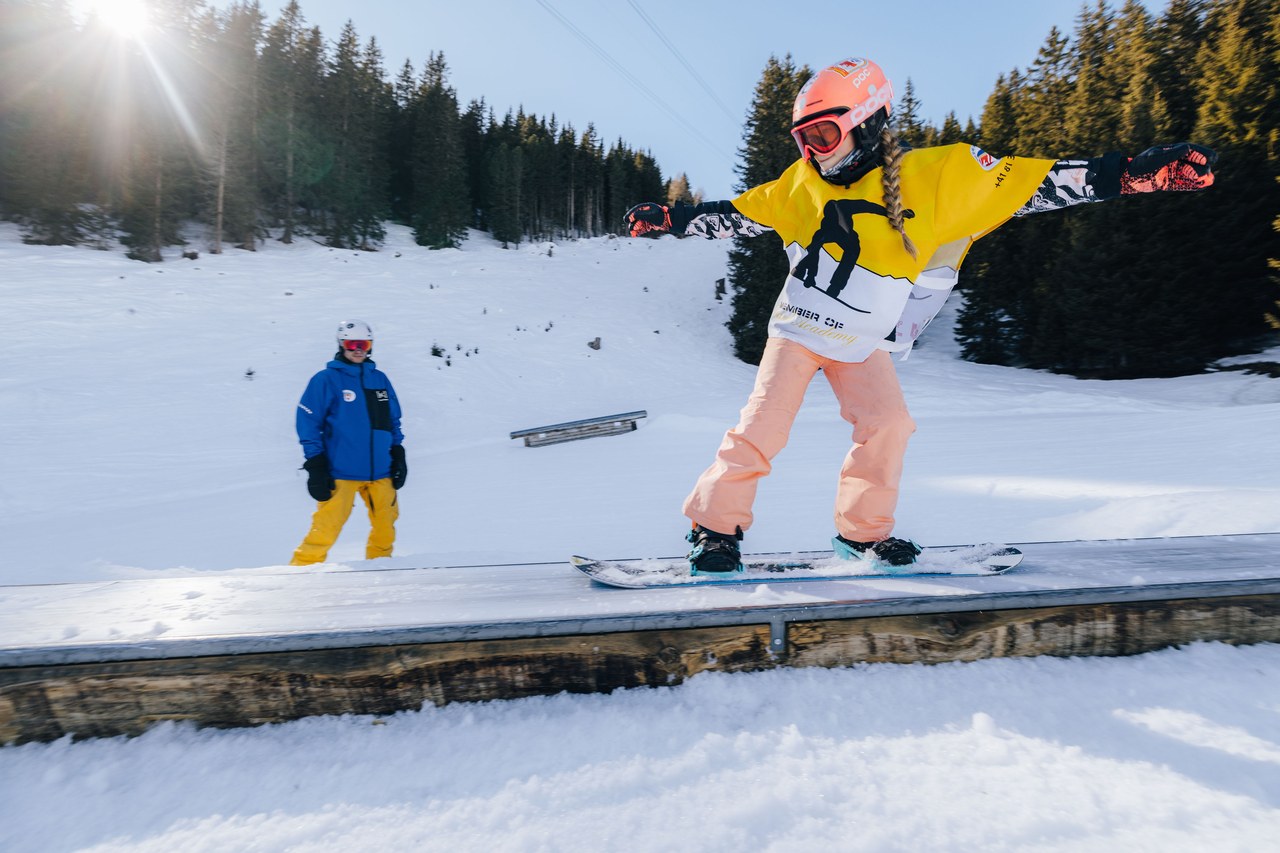 Kind der Skischule Arosa fährt mit dem Snowboard über eine Box im Snowpark